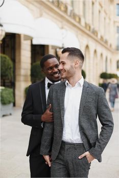 Afro american and caucasian happy handsome gays walking outside and holding hands in city. Concept of same sex male couple.