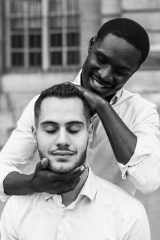 Black and white bw portrait in Paris. Afro american boy holding caucasian guy head by hands, wearing white shirt. Concept of stylish boy and haircut.