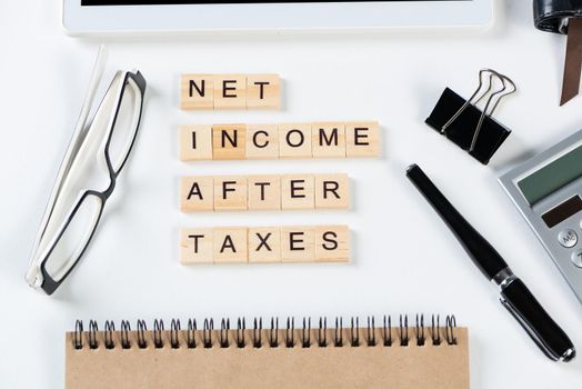 Net income after taxes concept with letters on cubes. Still life of office workplace with supplies. Flat lay white surface with tablet computer and calculator. Financial management and taxation.