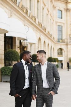Afro american and caucasian happy handsome gays walking outside and holding hands in city. Concept of same sex male couple.