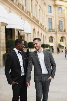 Afro american and caucasian stylish gays walking outside in city. Concept of same sex male couple.