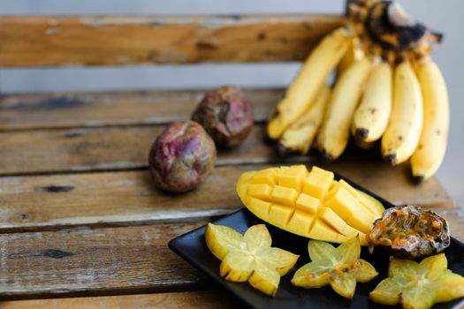 Close up tasty mango and carambola on plate near bananas on wooden table. Concept of tropical fruits and exotic healthy food.