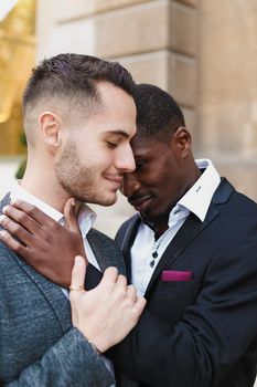 Afro american gay hugging caucasian boy outside, wearing suits. Concept of lgbt and same sex couple.