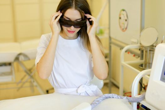 Young cosmetologist wearing special purpose glasses near permanent makeup device. Concept of beauty cosmetology salon and expensive high quality equipment.