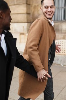 Caucasian smiling man in suit walking with afroamerican male person and hugging in city. Concept of happy lgbt gay and strolling.