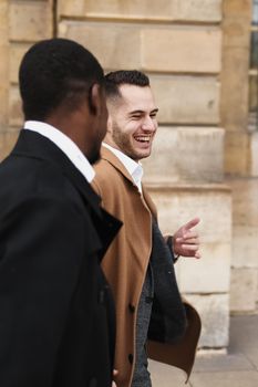 Caucasian smiling man in suit walking with afroamerican male person and hugging in city. Concept of happy lgbt gay and strolling.