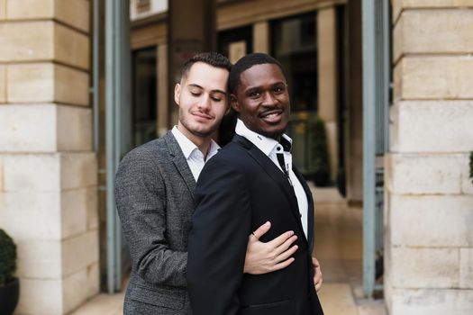 Caucasian man hugging afro american guy outside and wearing suit. Concept of happy same sex couple and lgbt gays.