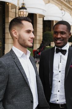 close up portrait of same sex couple. caucasian man wearing suit standing near afro american boy. Concept of business and male fashion.