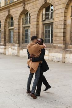 Caucasian smiling man in suit walking with afroamerican male person and hugging in city. Concept of happy lgbt gay and strolling.