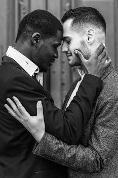 Black and white photo of caucasian man hugging afro american guy, wearing suit. Concept of relationship and same sex couple.