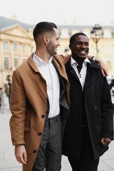 Caucasian smiling man in suit walking with afroamerican male person and hugging in city. Concept of happy lgbt gay and strolling.