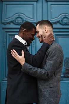 Afro american handsome man hugging caucasian guy in door background, wearing suit. Concept of same sex couple and gays.