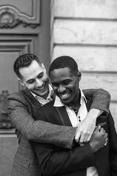 Black and white bw portrait Two boys, caucasian and afro american, wearing suits standing near building and hugging. Concept of gays and lgbt in Paris