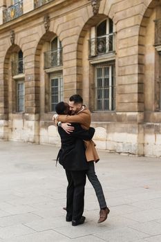 Caucasian smiling man in suit walking with afroamerican male person and hugging in city. Concept of happy lgbt gay and strolling.