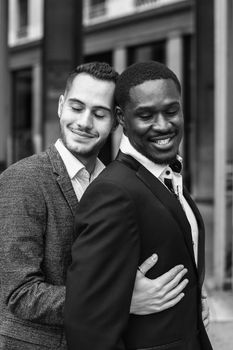 Black and white bw portrait Caucasian man hugging afro american guy outside and wearing suit. Concept of happy same sex couple and gays in Paris