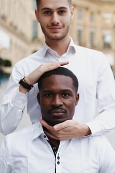 Caucasian boy holding afro american guy head by hands, wearing white shirt. Concept of stylish boy and haircut.