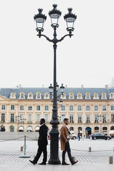 Afro american and caucasian boys standing near street lantern, wearing suits. Concept of urban photo session in Paris and life style.
