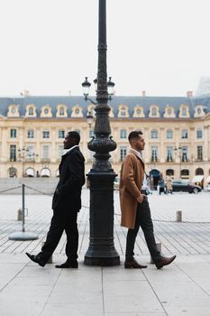 Afro american and caucasian boys standing near street lantern, wearing suits. Concept of urban photo session in Paris and life style.