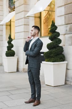 Young cacuasian male person wearing suit standing near building outdoors. Concept of fashion and businessman, urban life.