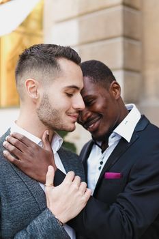 Afro american gay hugging caucasian boy outside, wearing suits. Concept of lgbt and same sex couple.