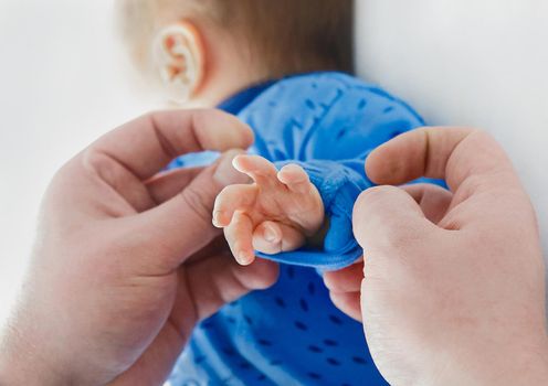 Dad's hands roll up sleeves on baby's hand, close-up. Newborn child in the hospital, love and care of the parent's dad.