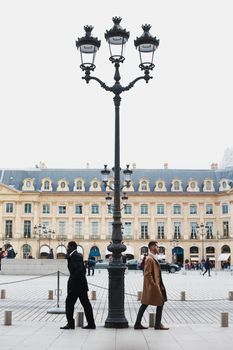 Afro american and caucasian boys standing near street lantern, wearing suits. Concept of urban photo session in Paris and life style.