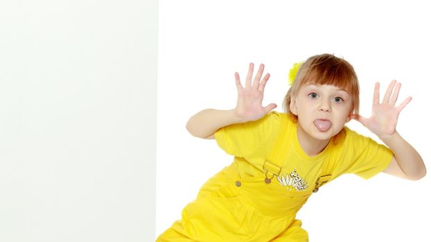 Girl with a short bangs on her head and bright yellow overalls.She crouched down on the white advertising banner.