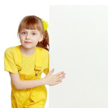 Girl with a short bangs on her head and bright yellow overalls.She crouched down on the white advertising banner.