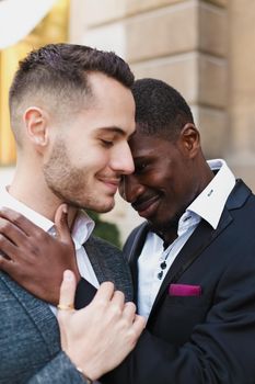 Afro american gay hugging caucasian boy outside, wearing suits. Concept of lgbt and same sex couple.