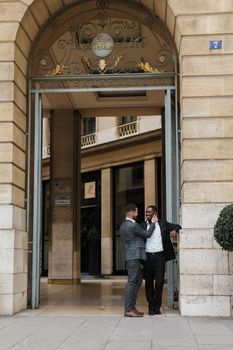 Two happy men, caucasian and afro american, wearing suits speaking near building outdoors. Concept of successful business partners.