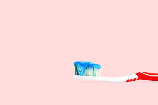 Closeup a blue and white toothpaste on a toothbrush isolated on pink color background.