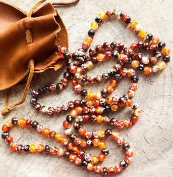 Sunny beads of amber fireplace faceted agate with leather jewelry pouch bag on rustic background