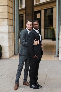 Caucasian man hugging afro american guy outside and wearing suit. Concept of happy same sex couple and lgbt gays.