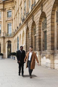 Caucasian smiling man in suit walking with afroamerican male person and hugging in city. Concept of happy lgbt gay and strolling.