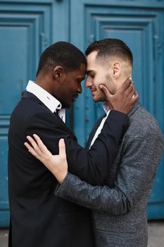 Afro american handsome man hugging caucasian guy in door background, wearing suit. Concept of same sex couple and gays.