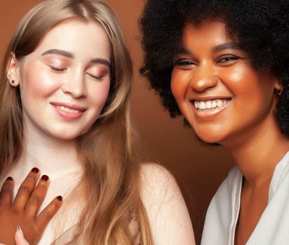 young pretty african and caucasian women posing cheerful together on brown background, lifestyle diverse nationality people concept close up