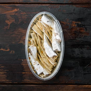 Canned Anchovy set, in plastic container, on old dark wooden table background, top view flat lay, square format