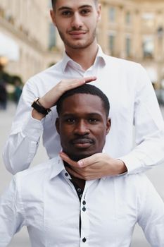 Caucasian boy holding afro american guy head by hands, wearing white shirt. Concept of stylish boy and haircut.