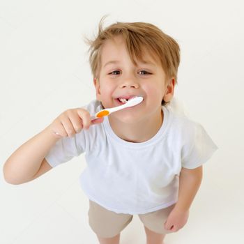 A cute little boy is brushing his teeth with a toothbrush. On a pure white T-shirt in which he is dressed you can make an advertising inscription. The concept of children's health, medicine. Isolated on white background.