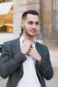 Young cacuasian male person wearing suit standing near building outdoors. Concept of fashion and businessman, urban life.