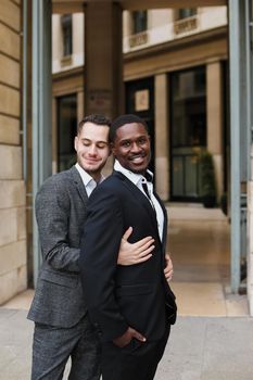 Caucasian man hugging afro american guy outside and wearing suit. Concept of happy same sex couple and lgbt gays.