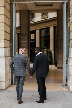 Two men, caucasian and afro american, wearing suits talking near building outside and hugging.