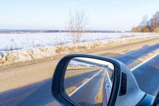 View in early spring, when there is still snow, on the asphalt road through the rear-view mirror of the car.