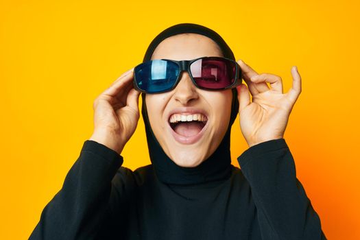 cheerful woman in black hijab popcorn 3D glasses cinema yellow background. High quality photo