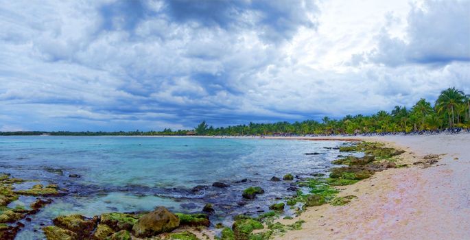 View of the turquoise ocean with a tropical beach, with green vegetation and white sand. Through the dense leaves of palm trees blue sky and sun. Summer holidays on the islands.