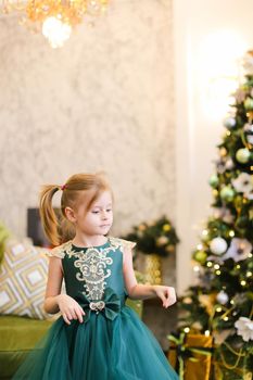 Little girl wearing dress and standing with bengal lights near Christmas tree. Concept of celebrating winter holidays and childhood.