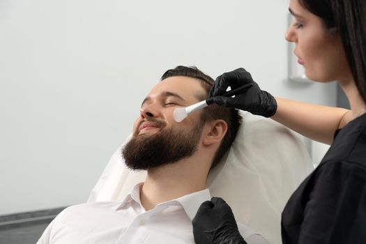 Bearded man getting laser facial treatment by professional cosmetologist in beauty clinic. Healthy man lifestyle concept