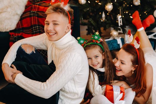 a happy family is lying on the floor of the house with New Year's gifts, next to the Christmas tree,