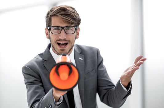 Portrait of furious business man screaming with megaphone in modern office. The angry man looks at camera. Copy space
