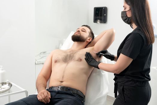 Doctor doing injection from hyperhidrosis to armpit. Man receiving underarm treatment in cosmetology clinic
